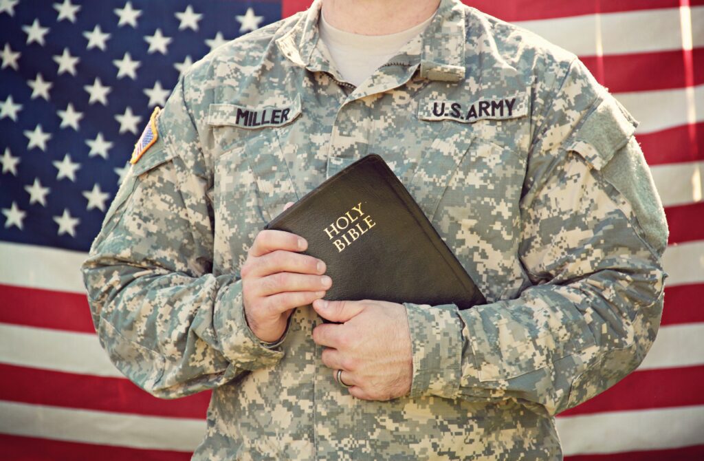 A soldier holding an army bible in front of the american flag.