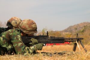 A soldier is sitting in the grass with his rifle.