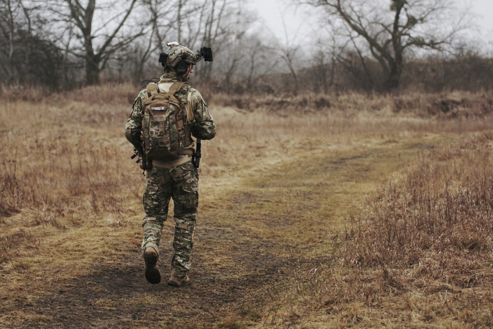 A man in camouflage walking on the side of a dirt road.